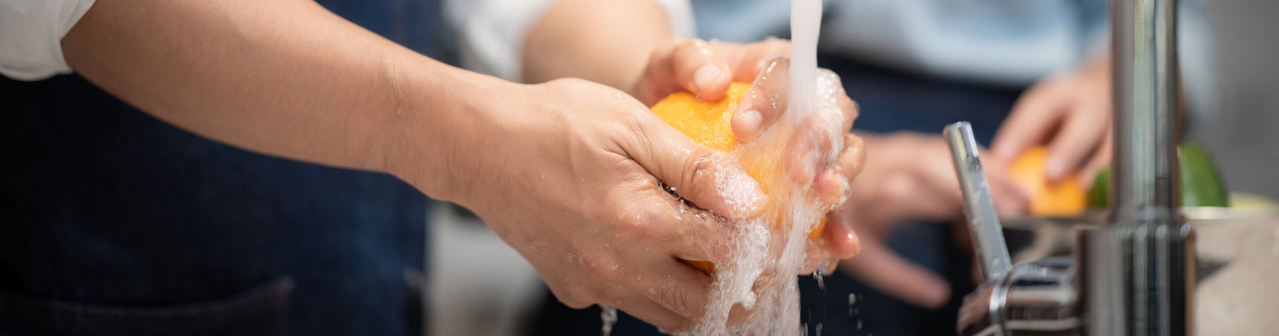 A person washing a yellow pepper under a sink