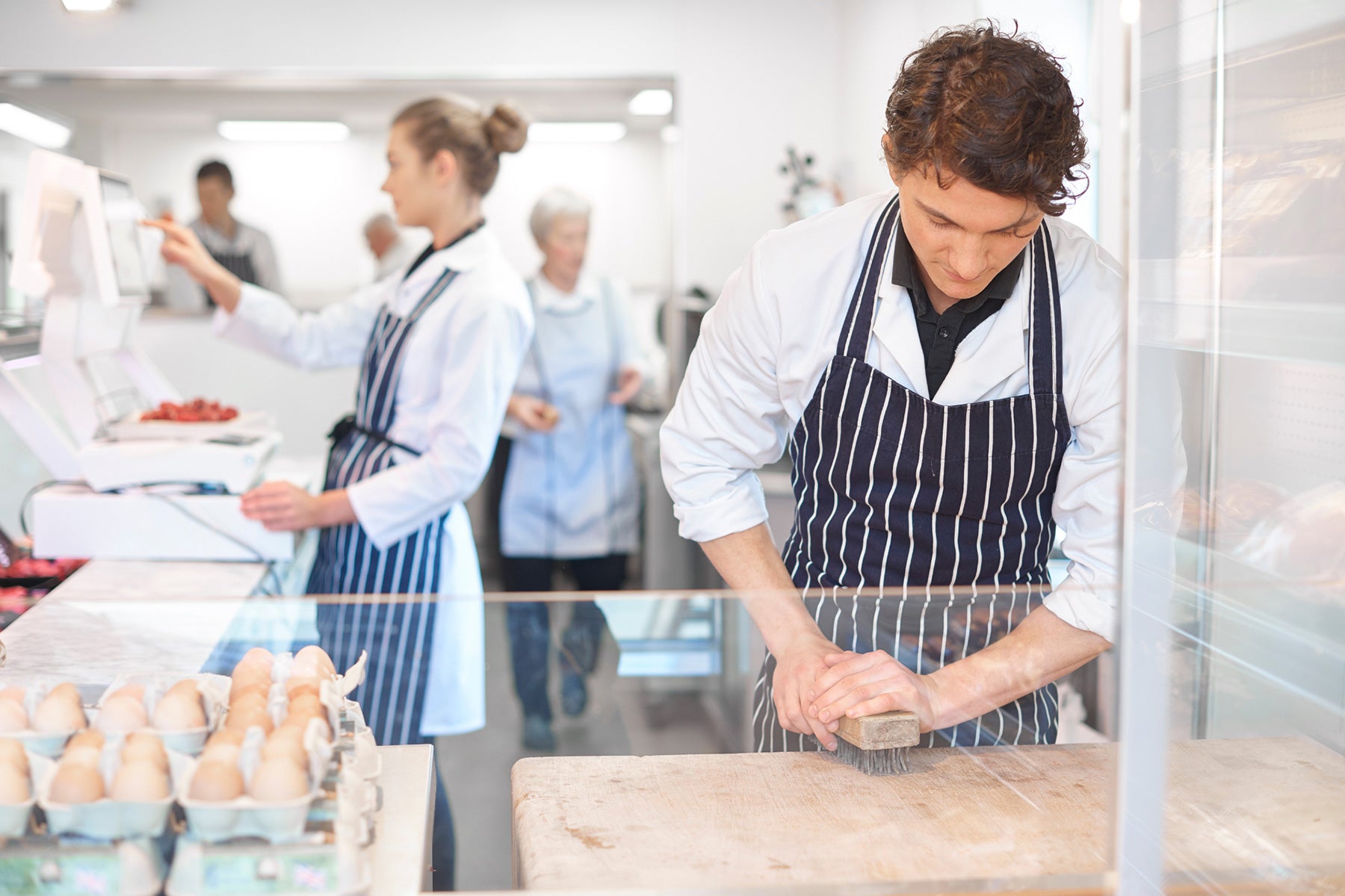 A butcher in an apron uses a soft brush to maintain butcher block countertops