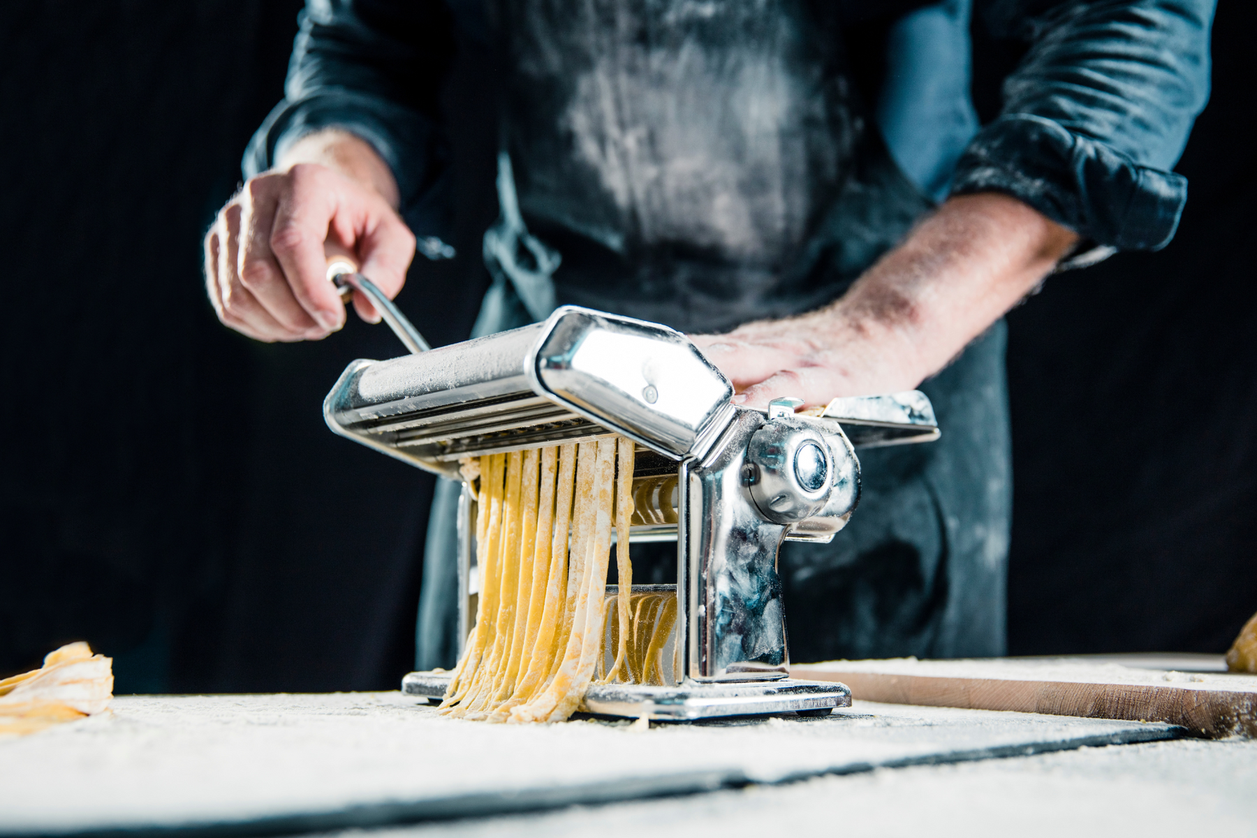 A chef wearing all black making fresh pasta using a manual pasta maker