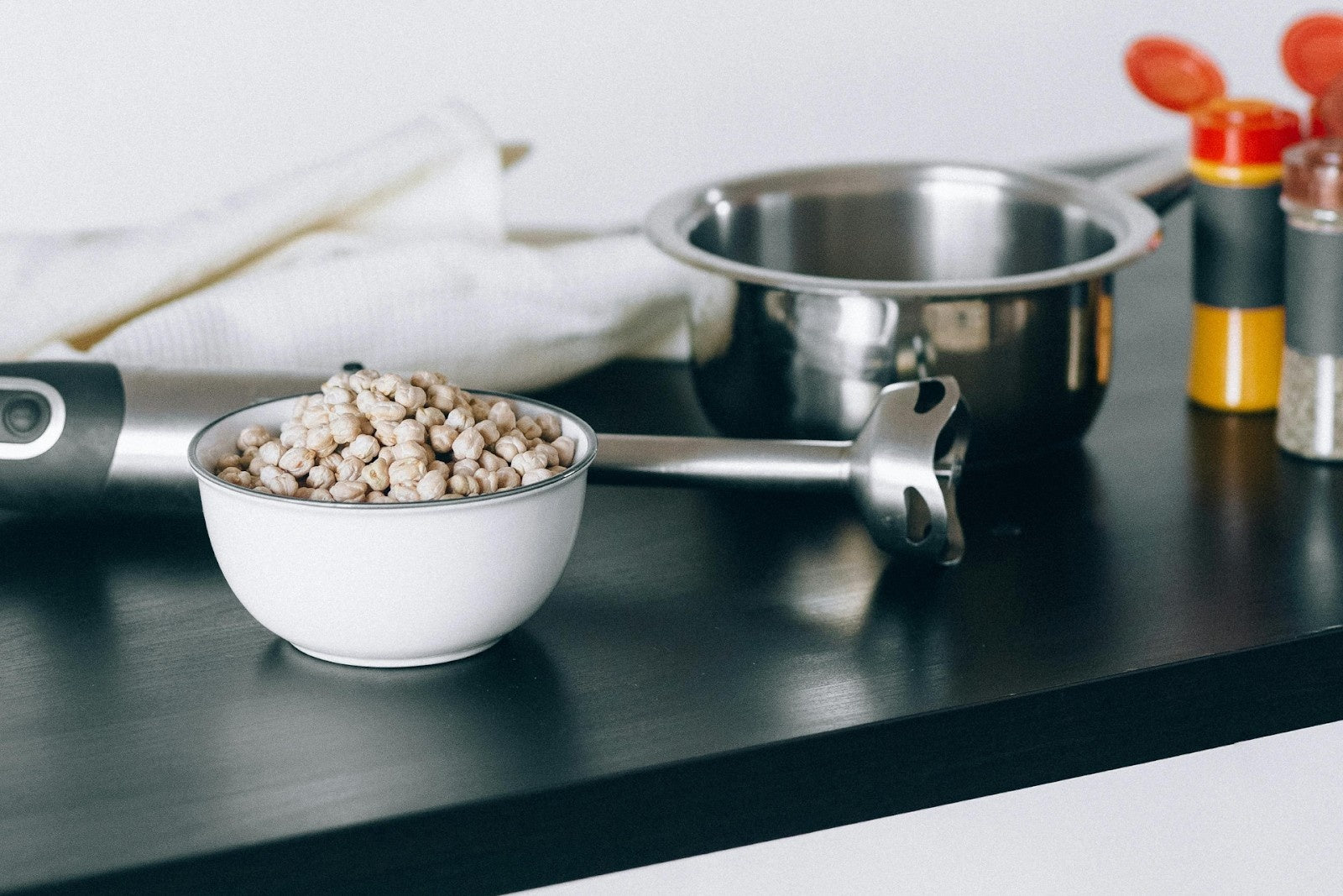 Stainless steel immersion blender for meal prep, next to a bowl of chickpeas on a countertop.