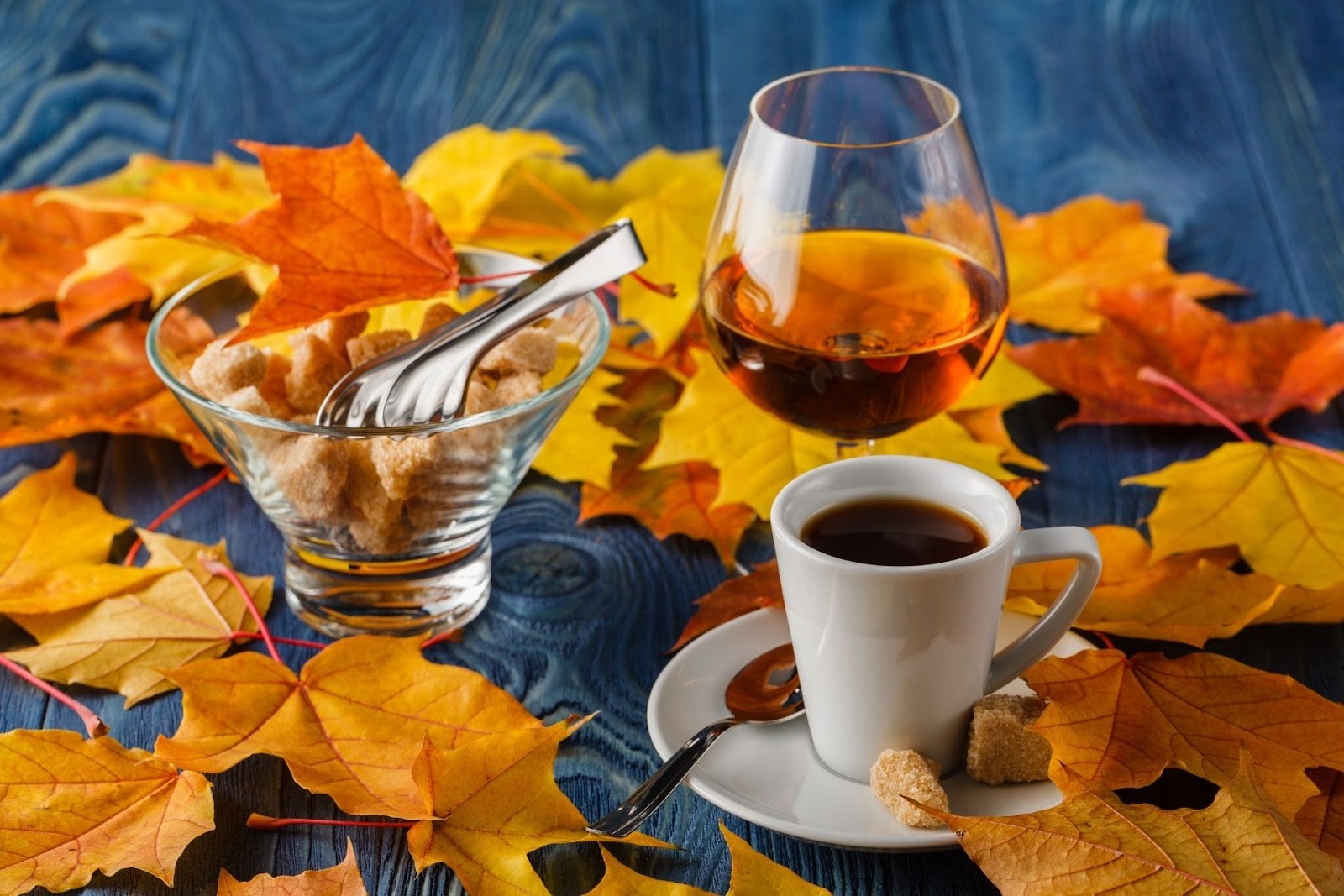 Autumn coffee, brandy, brown sugar, and red maple leaves on a wooden table 